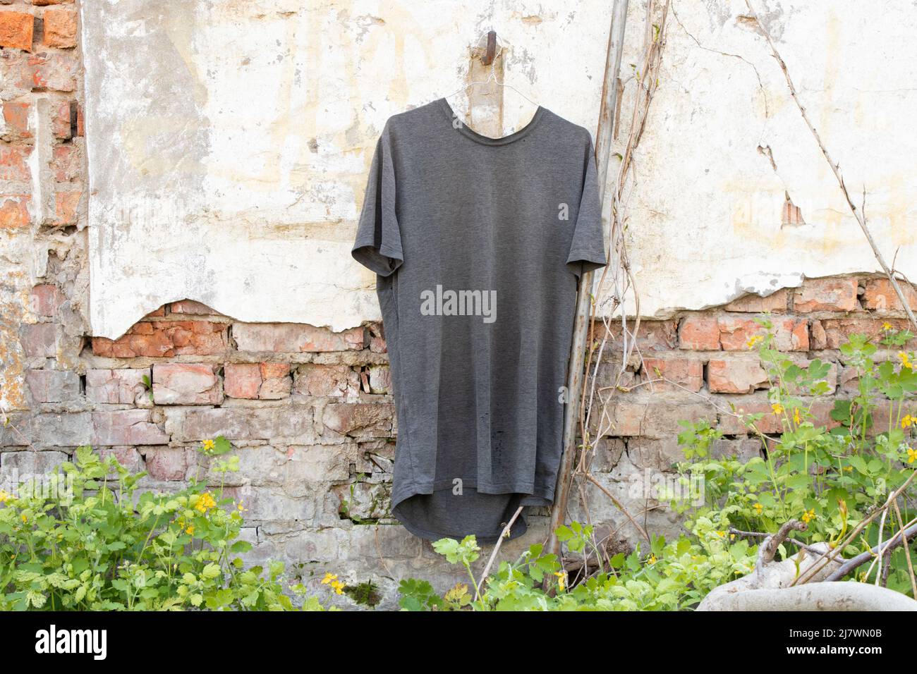 Gray t-shirt on hangers hanging on the wall in the street in the sun, fashion and trends Stock Photo