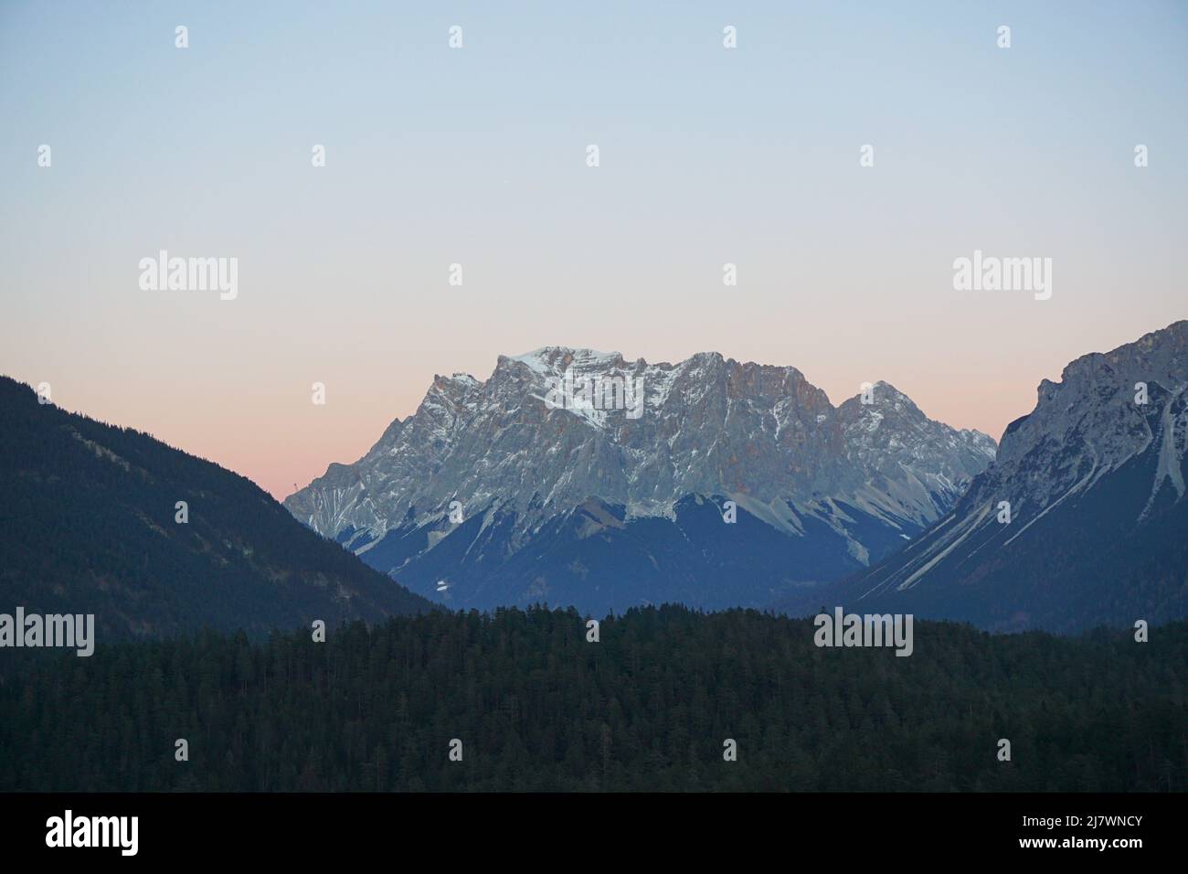 Panoramic view of the rocky Zugspitze peak, with forest in front and beautiful sunset sky in the back, shot in December Stock Photo