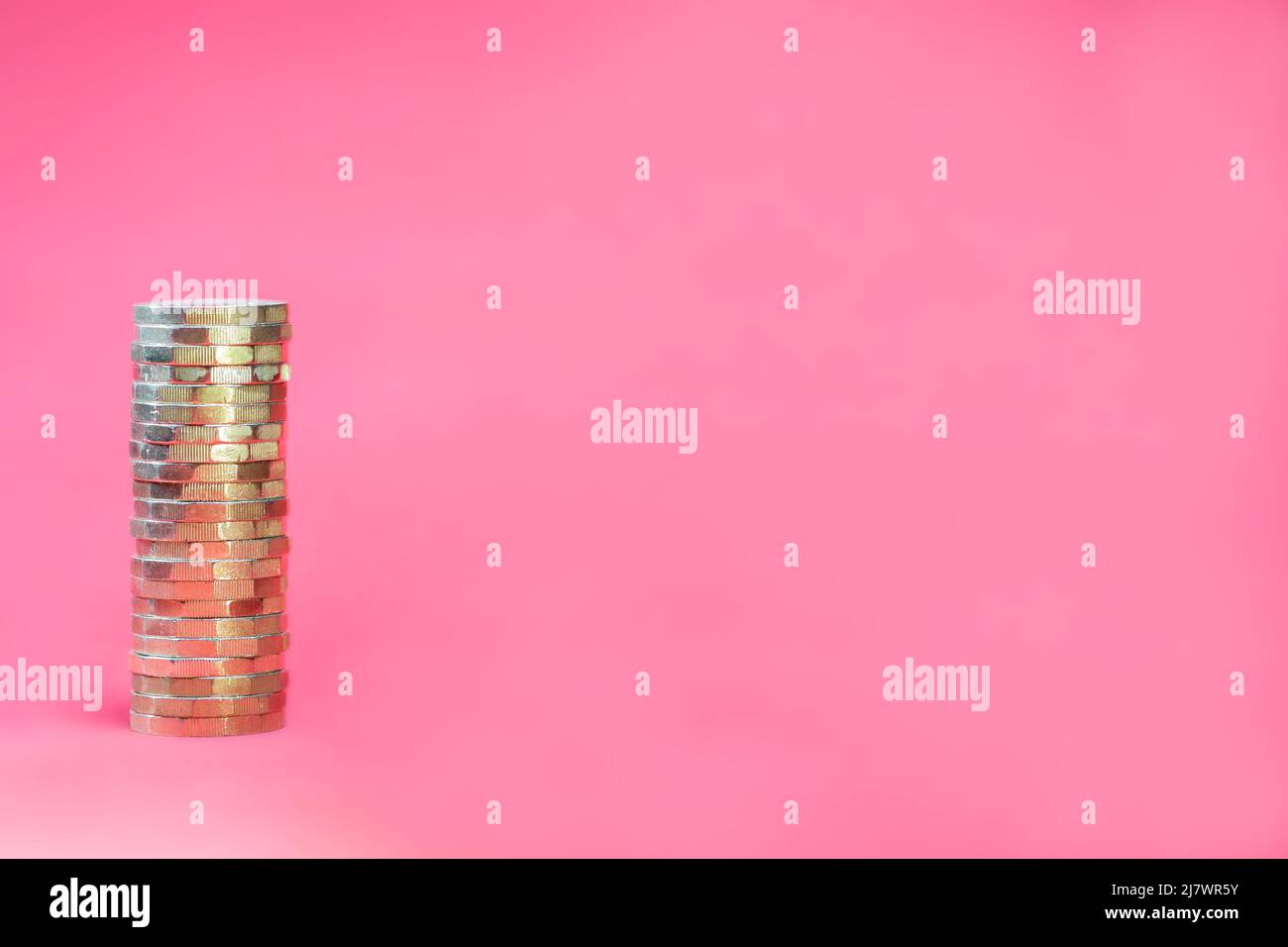 Single stack of gold coloured UK GBP sterling pound coins positioned left on a bright pink fuchsia background with copy space. Savings and Investments Stock Photo