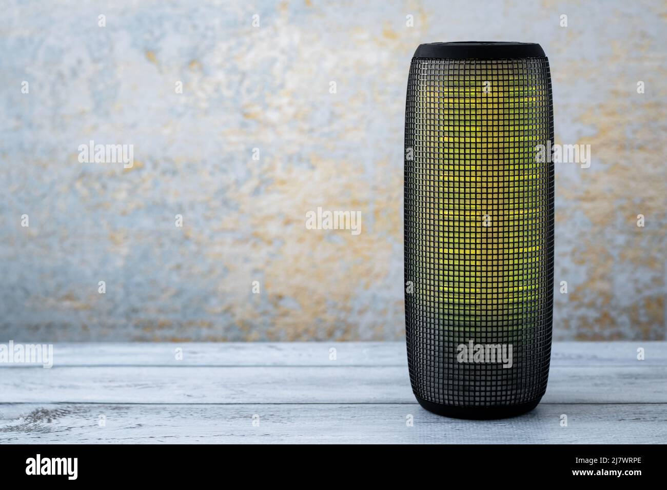 A portable music column on wooden gray background. Musical wireless speaker with yellow glow. Sound system. Single object. Copy, text space Stock Photo