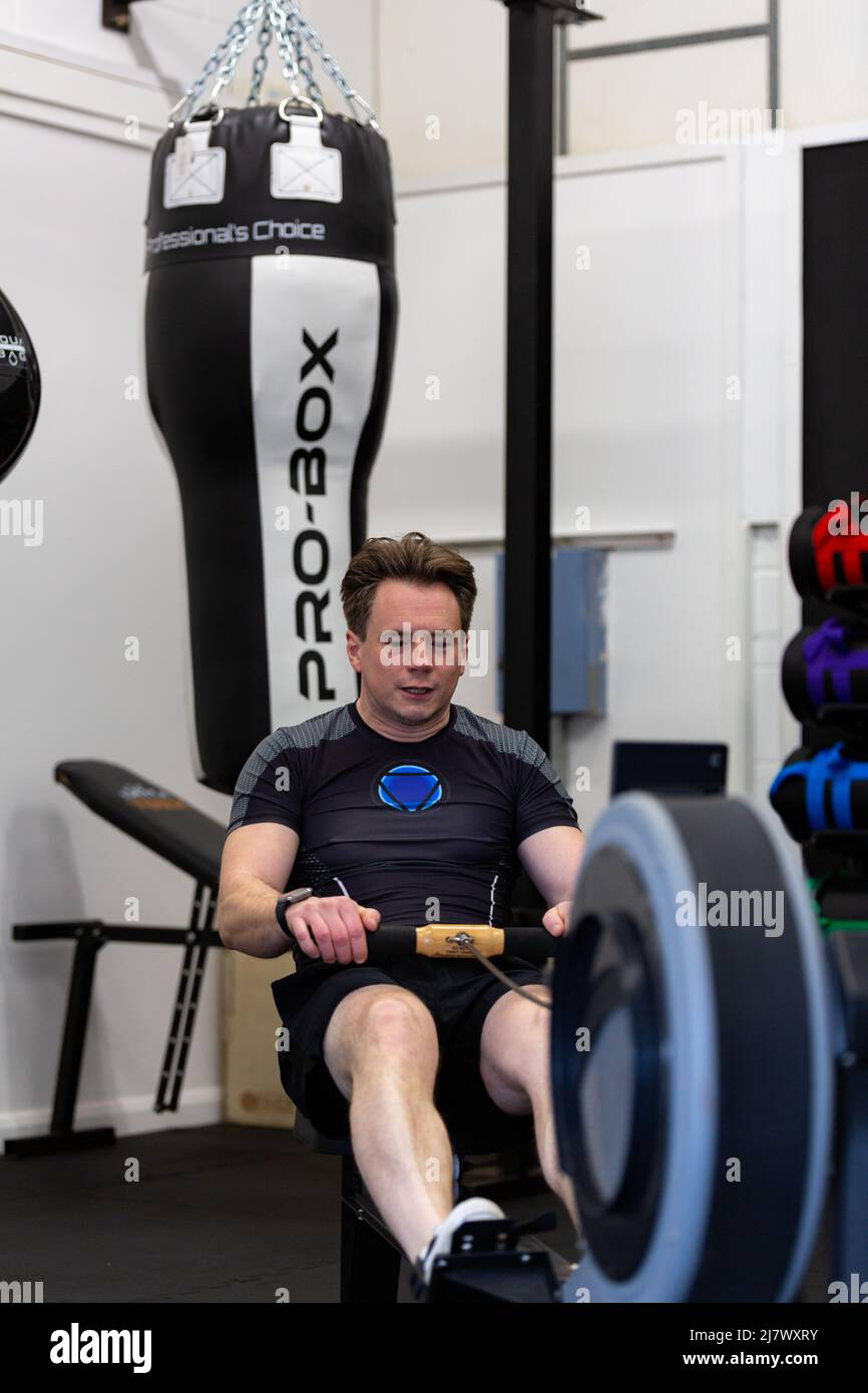 Ipswich Suffolk UK April 03 2022: A fit and healthy young man using a rowing machine in a small gym Stock Photo