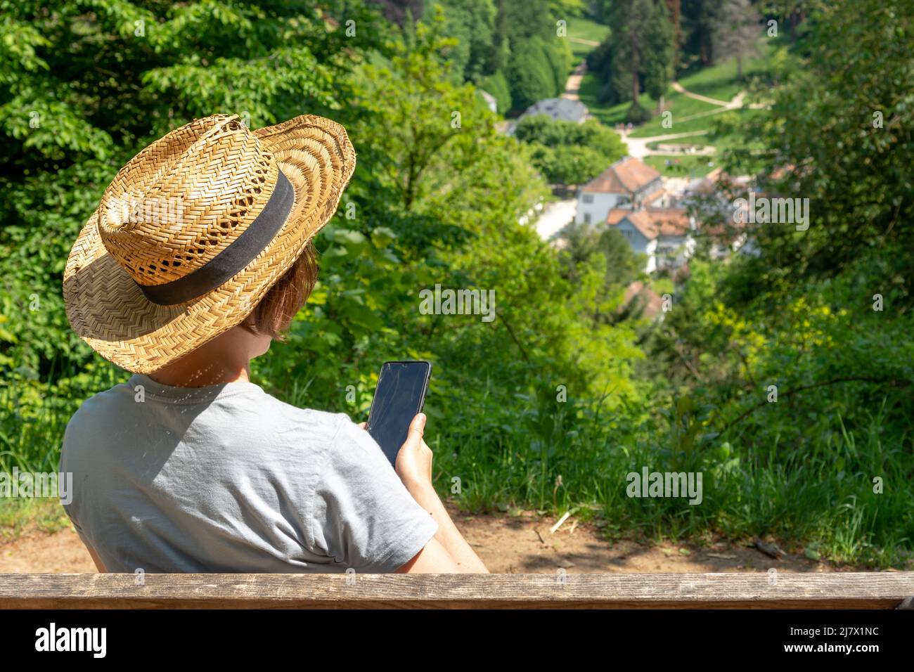 Woman with brown hair, straw hat and gray color t-shirt sitting on a park  bench, looking at her phone with broken device screen, Staatspark  Fürstenlag Stock Photo - Alamy