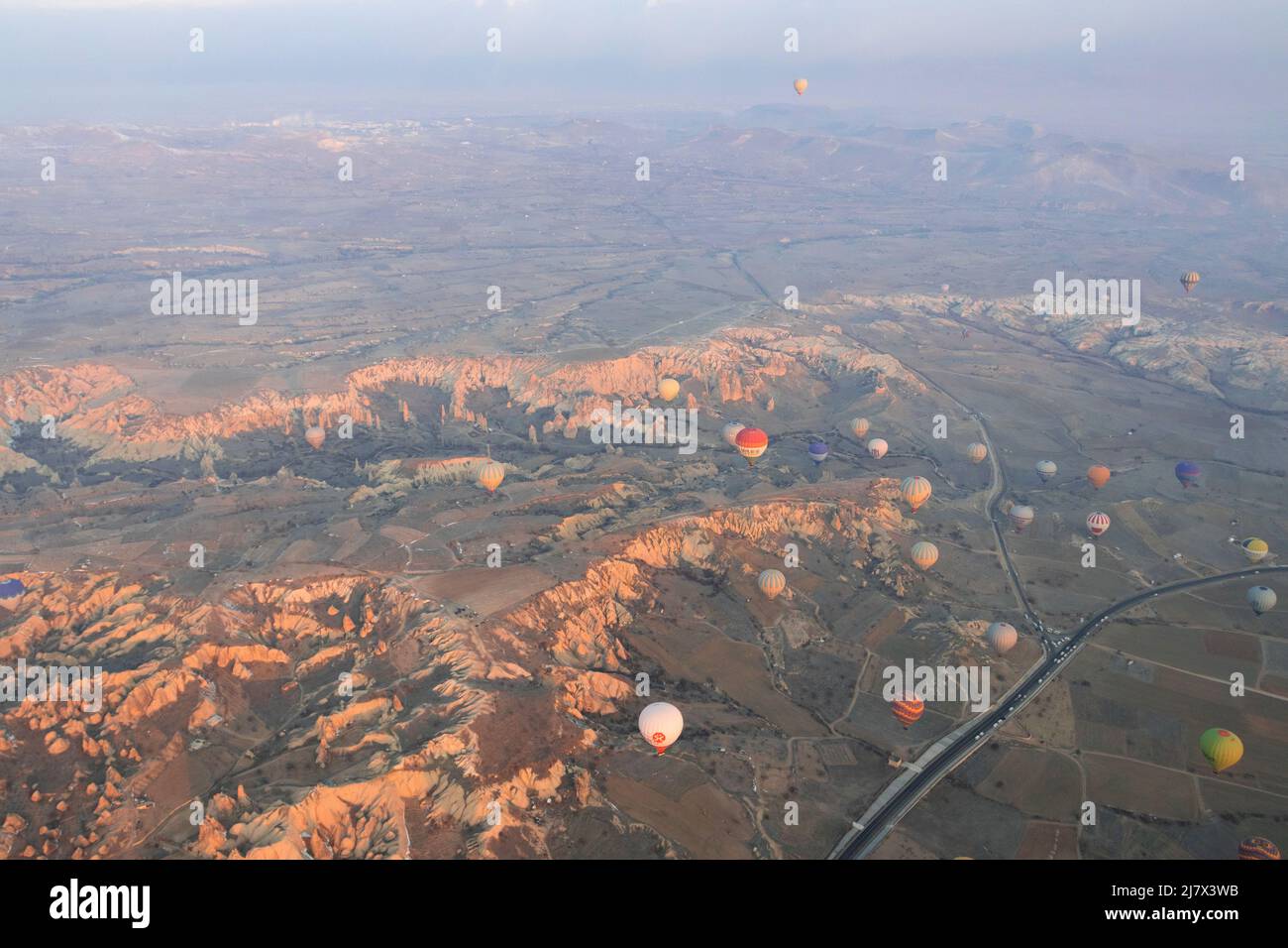 Hot air balloons are flying over the valley with road in Cappadocia ...