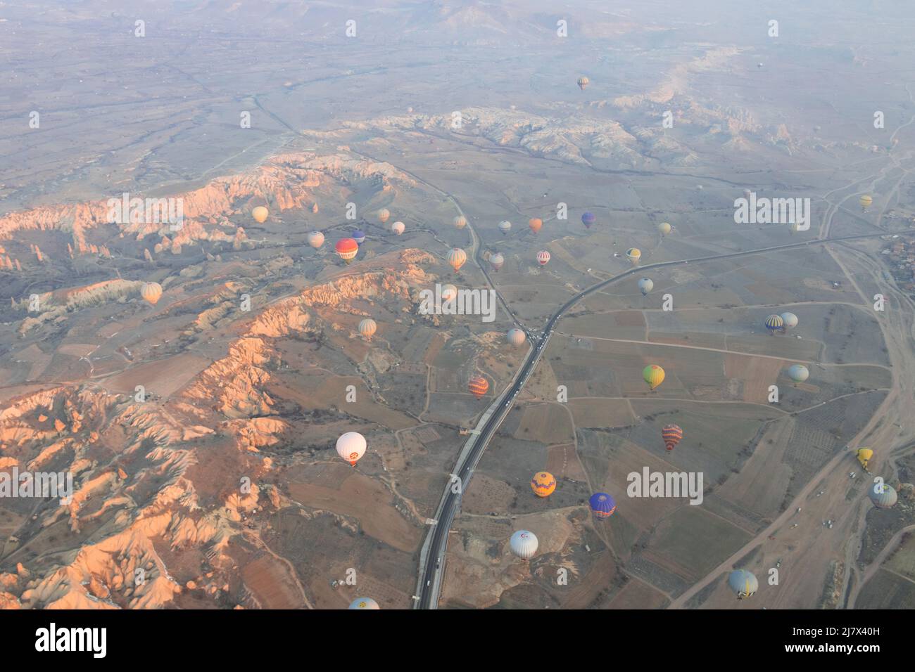 A lot of hot air balloons are flying over the valley with road in ...