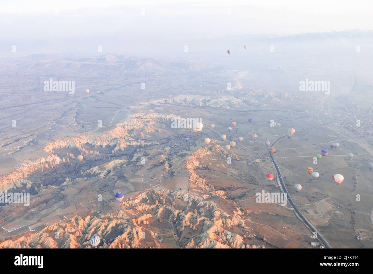 Hot air balloons are flying over the valley with road in Cappadocia ...