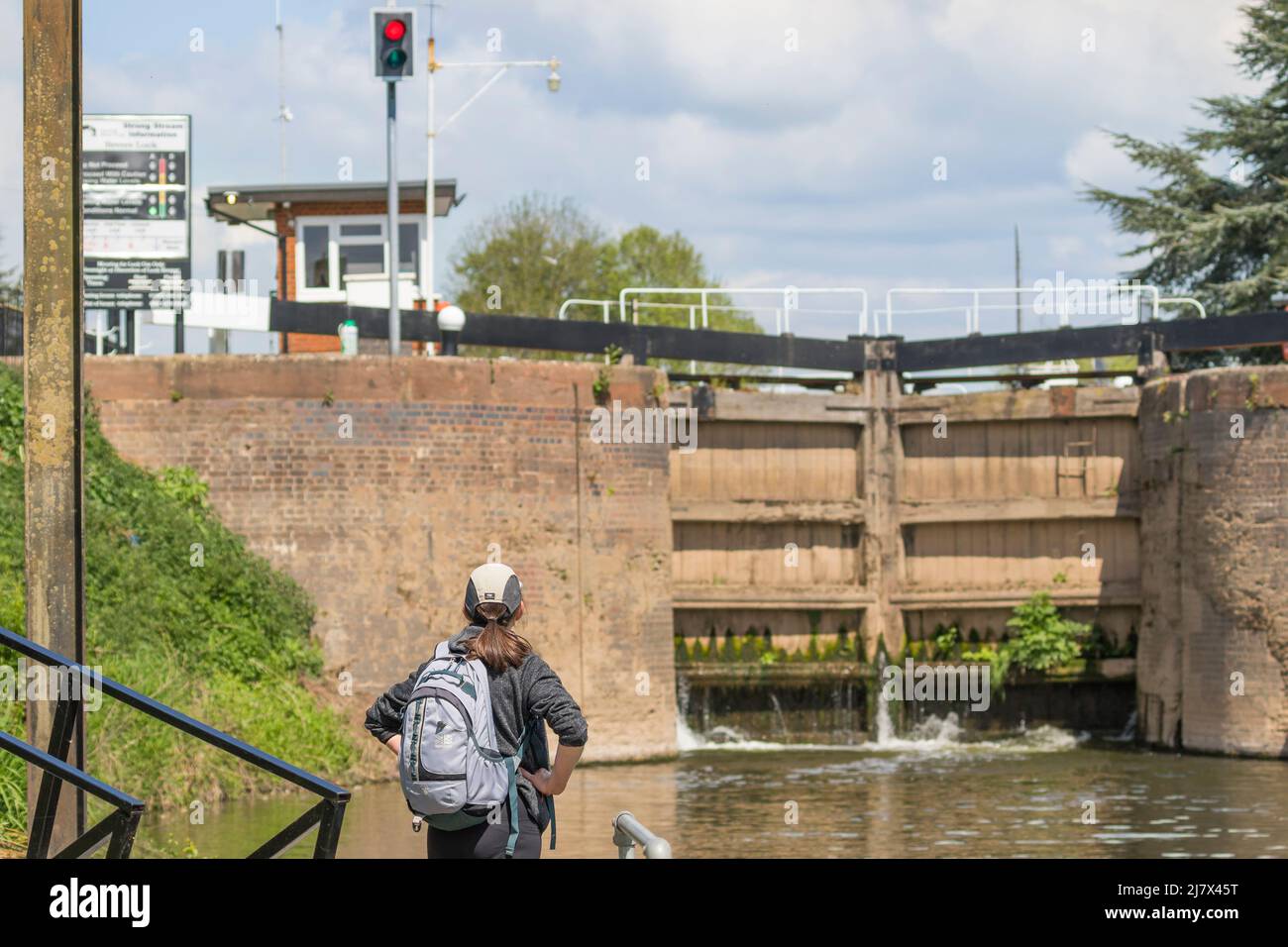 Rear view of a woman hiker looking at a set of closed automated river lock gates, Bevere Lock, Worcestershire, UK (focus on woman). Stock Photo