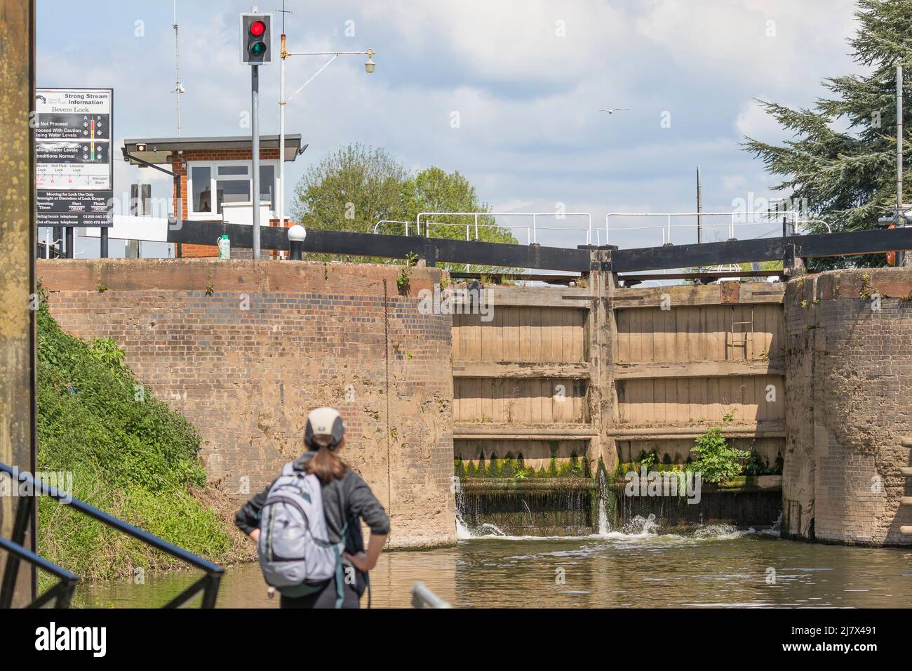 Rear view of a woman hiker looking at a set of closed automated river lock gates, Bevere Lock, Worcestershire, UK (focus on lock gates). Stock Photo