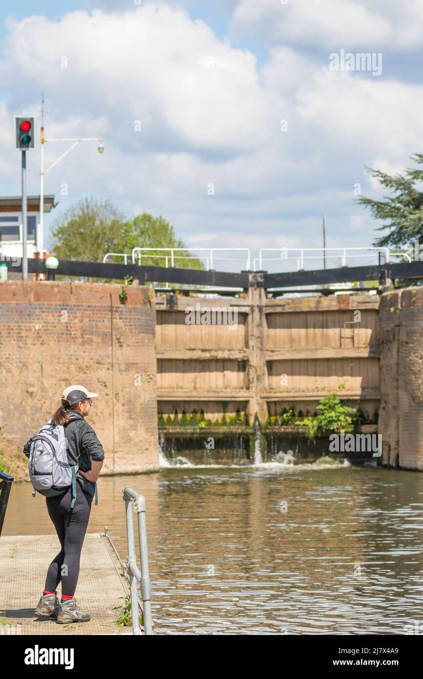 Rear view of a woman looking at a set of closed automated river lock gates, focus is on the woman hiker Stock Photo