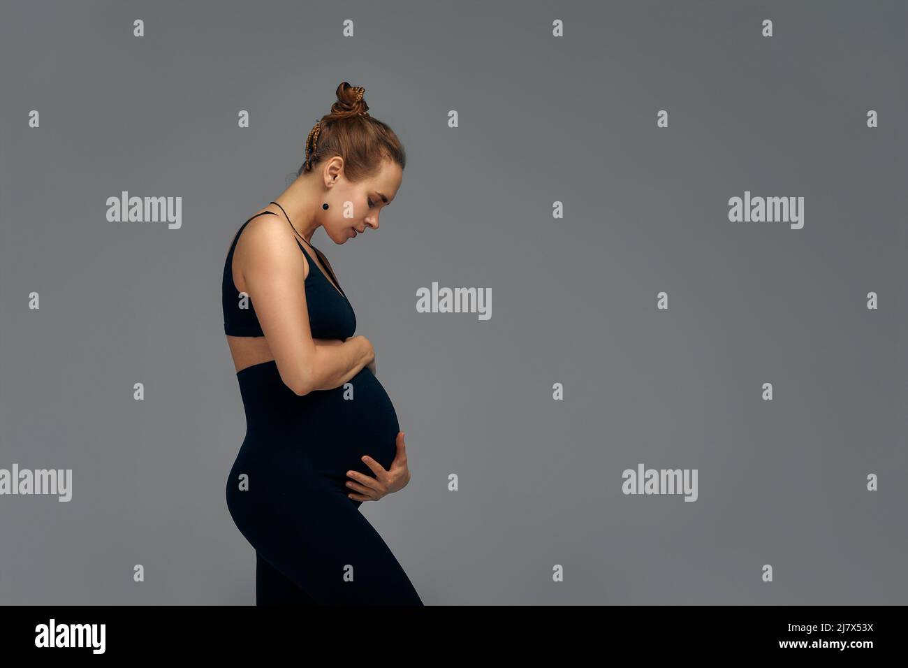 Cute pregnant belly isolated on gray. Side view of young pregnant woman