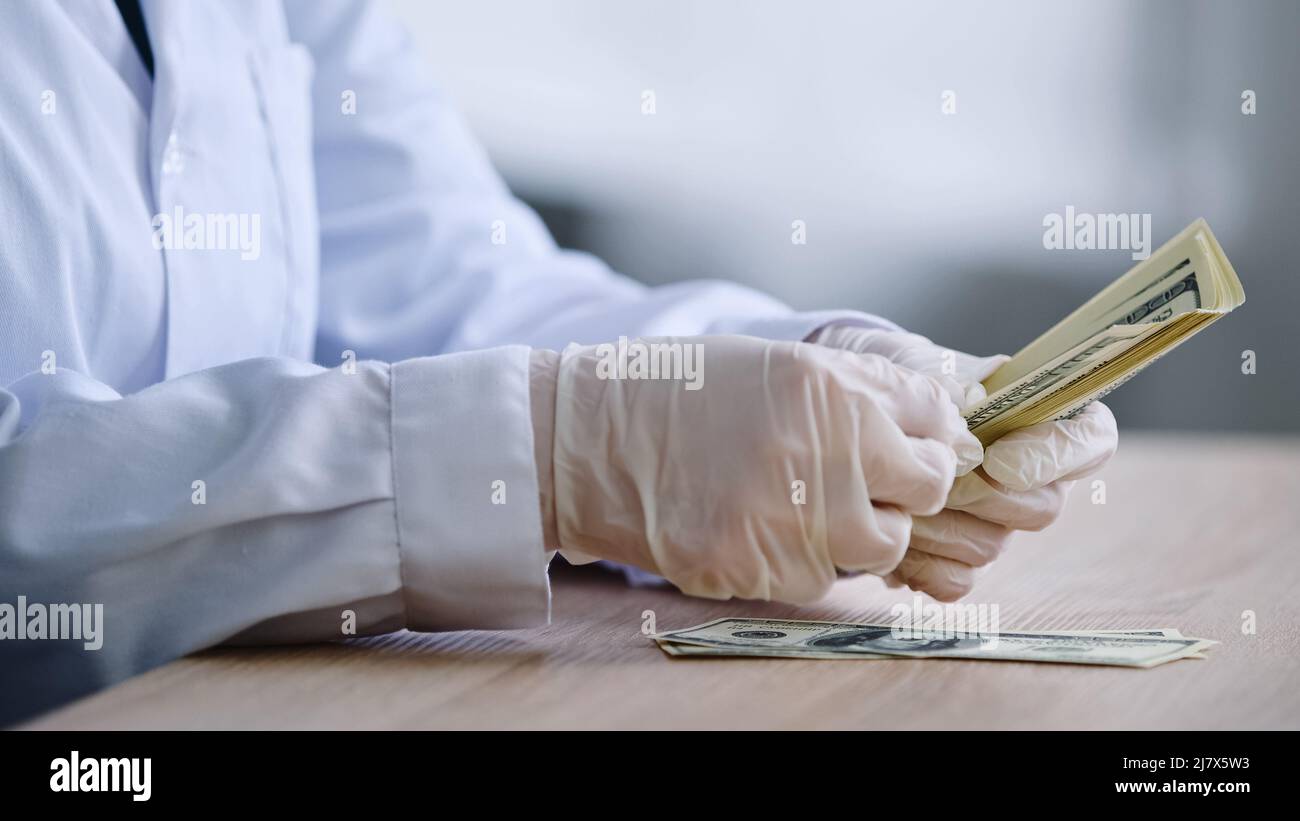 Close-up female hands in white latex gloves pharmacist doctor scientist in medical coat sits at table with bottle of pills drug counting money Stock Photo