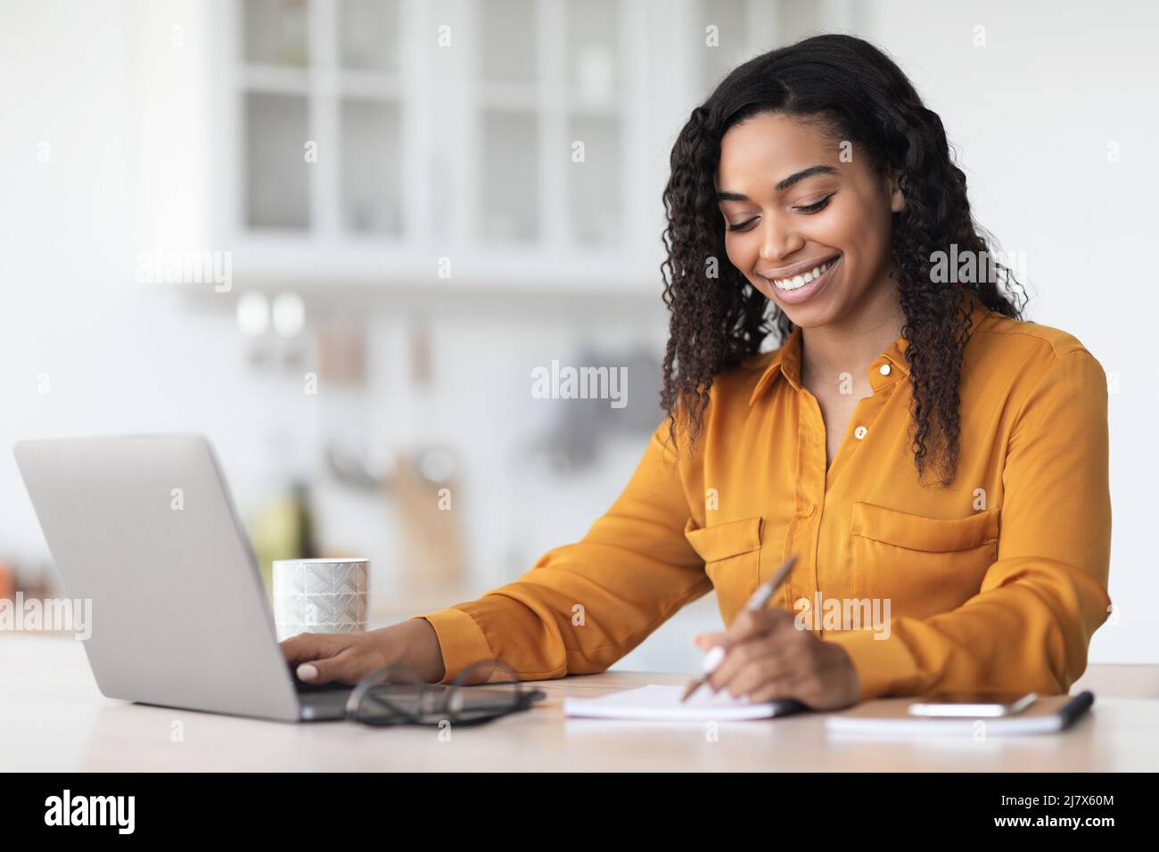 Cheerful pretty black lady working from home, taking notes Stock Photo