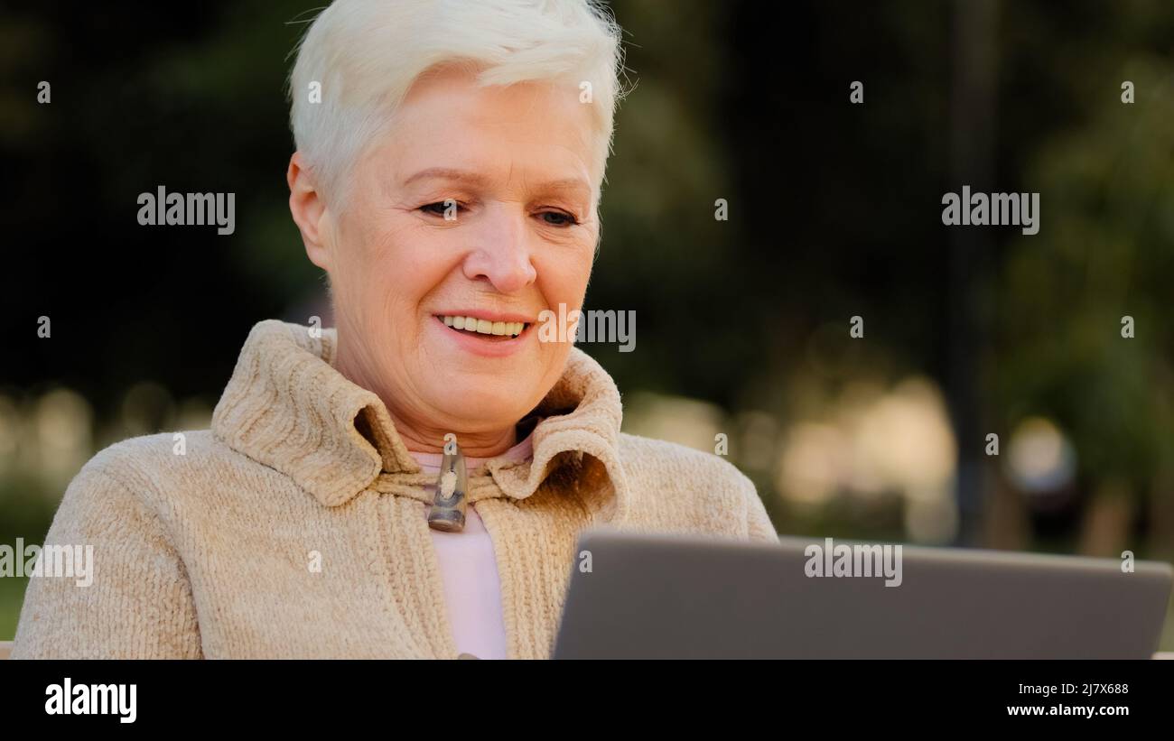 Happy aged woman working at laptop smiling senior female of retirement age using computer browsing or surfing internet, reading news online, excited Stock Photo