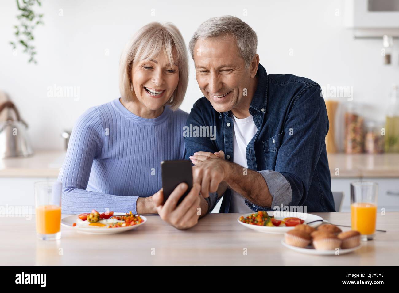 Happy senior couple using smartphone while having breakfast Stock Photo