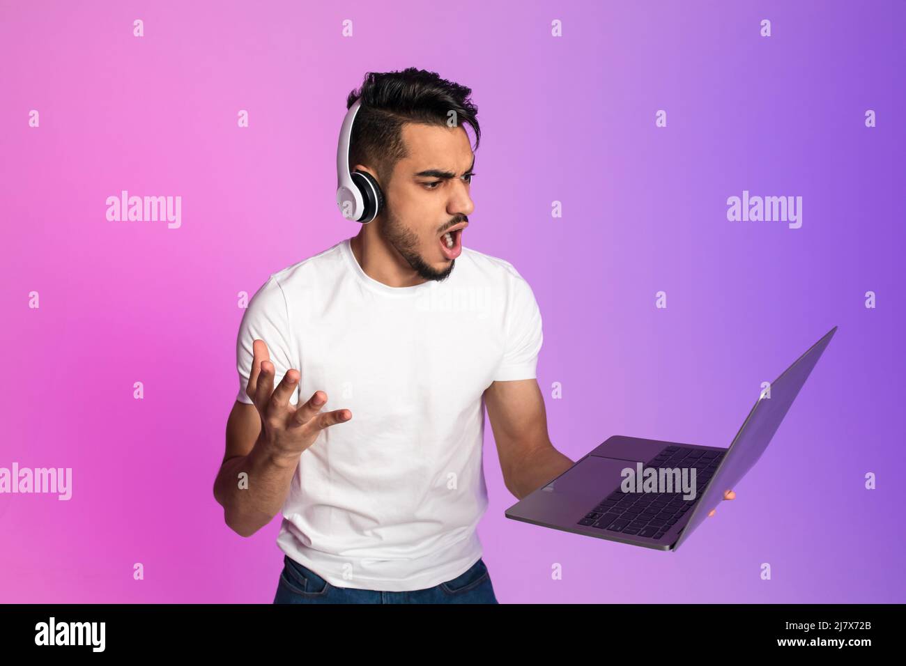 Angry young Arab man in headphones shouting at laptop computer, feeling ...