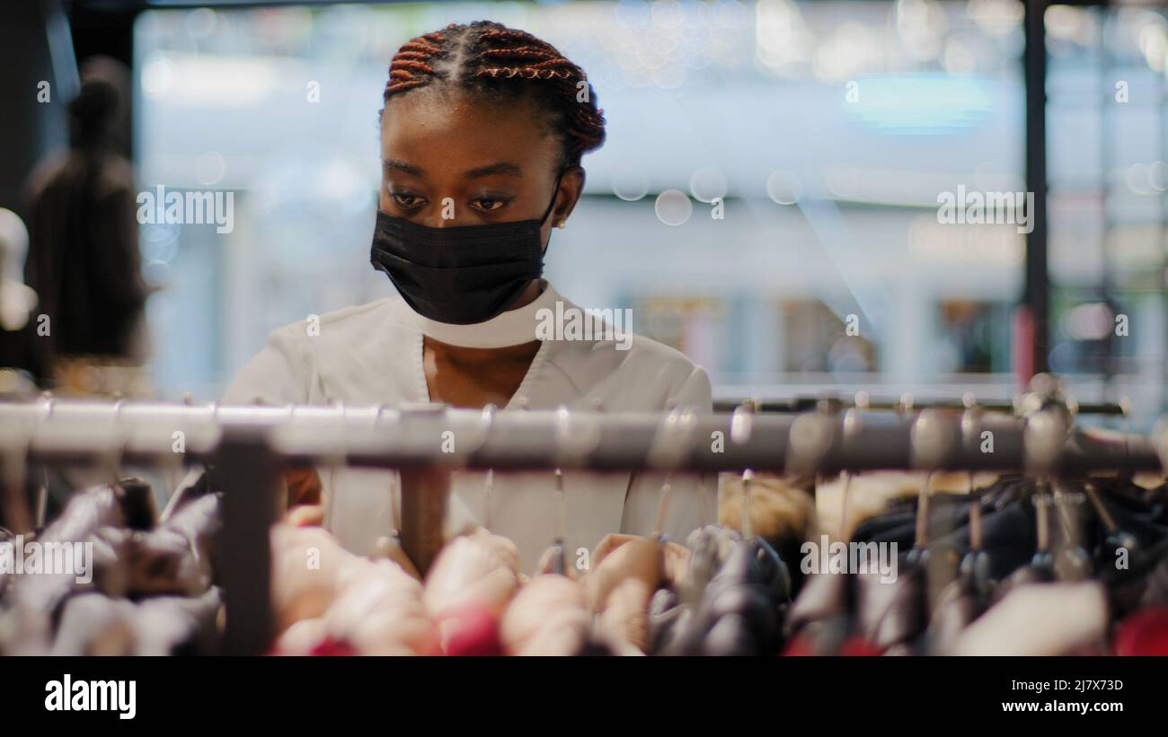 Young fashion trendy african american girl attractive shopper consumer client wearing medical mask chooses clothes choosing outfits in store Stock Photo