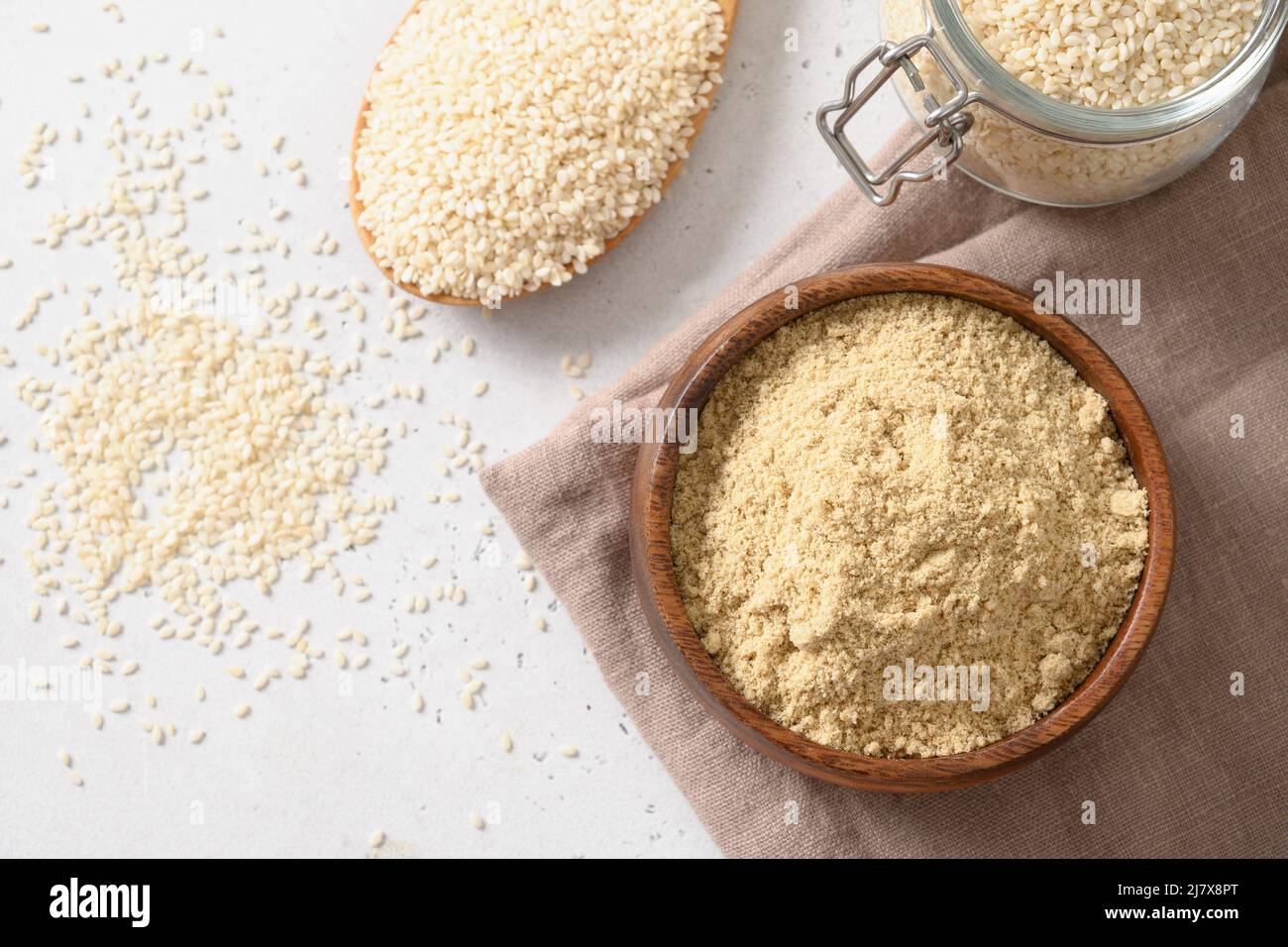 Sesame flour in bowl and sesame seeds in spoon on white background. Top view. Copy space. Sesame flour includes ample minerals, natural antioxidants a Stock Photo
