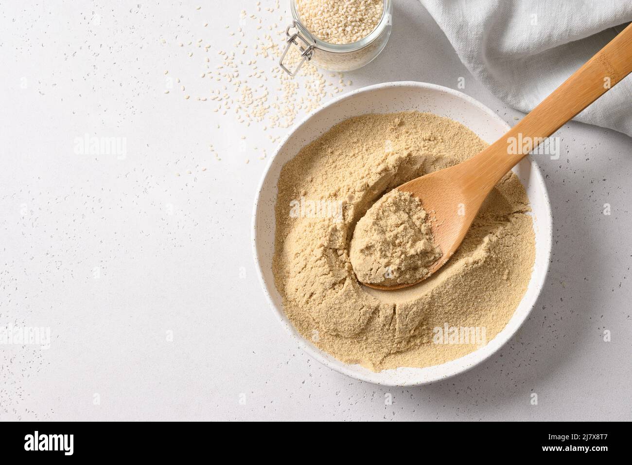 Sesame flour in white bowl and sesame seeds in spoon on white background. Top view. Copy space. Good source of protein, minerals, natural antioxidants Stock Photo