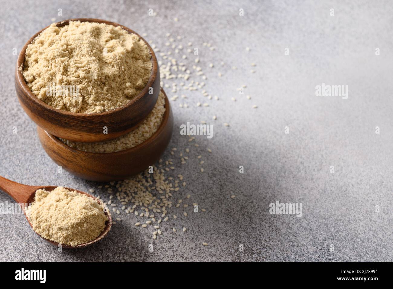 Sesame flour in wooden bowls and spoon on gray background for cooking gluten-free and low carbohydrate dessert. Good source of protein, minerals, natu Stock Photo