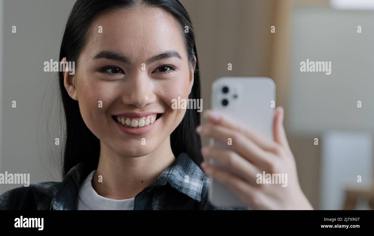 Happy asian korean Japanese Chinese girl smiling female face woman with mobile phone waving hand talking to webcam make video call at home talking Stock Photo