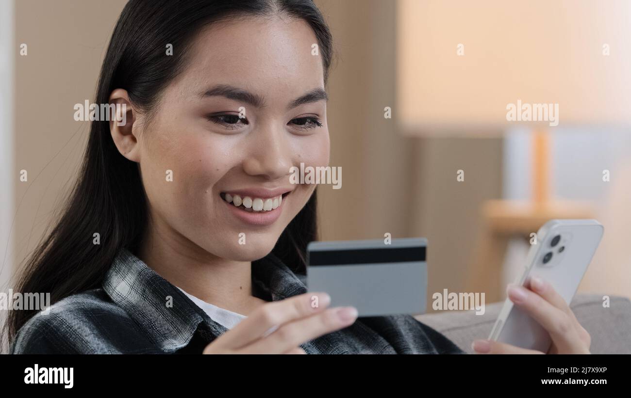 Asian Korean Japanese Chinese girl millennial woman with bank credit card and mobile phone making transaction online electronic payment shopping Stock Photo