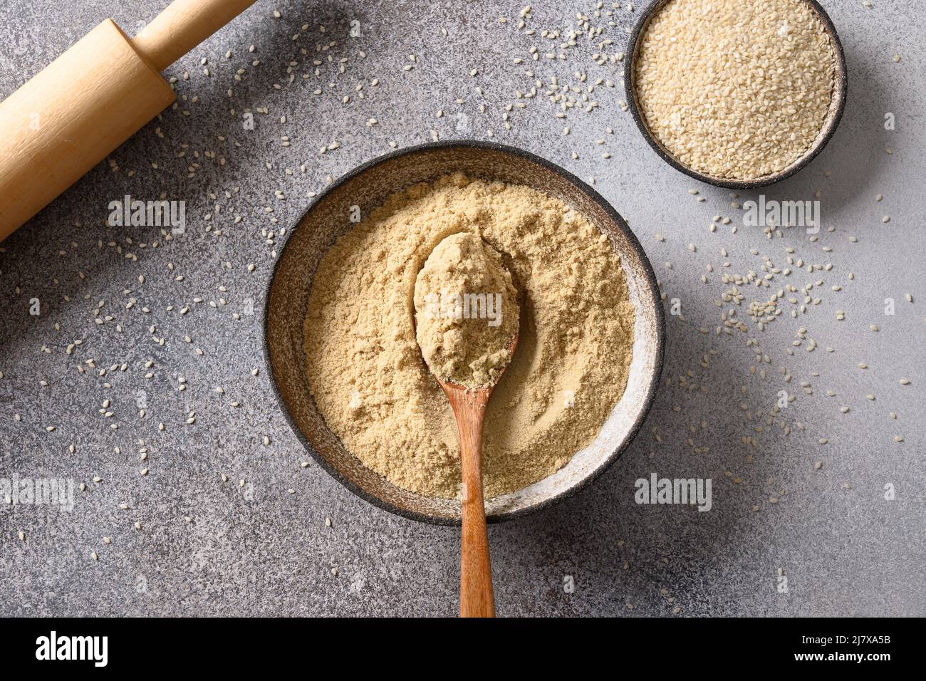 Sesame flour in bowl and white sesame seeds on gray background for cooking gluten free dessert. View from above. Good source of protein, minerals, nat Stock Photo