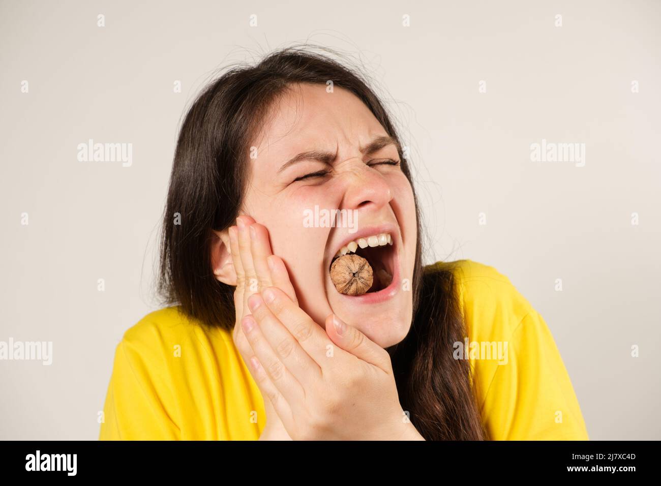 A woman gnaws on a walnut, opening her mouth wide, breaking a tooth or dislocating the temporomandibular joint, her jaw has moved away. Stock Photo