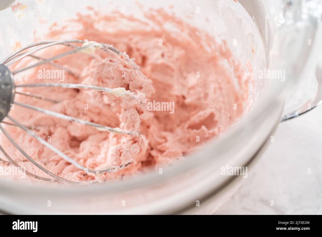 Whipping strawberry buttercream frosting in a standalone electric mixer with a whisk attachment