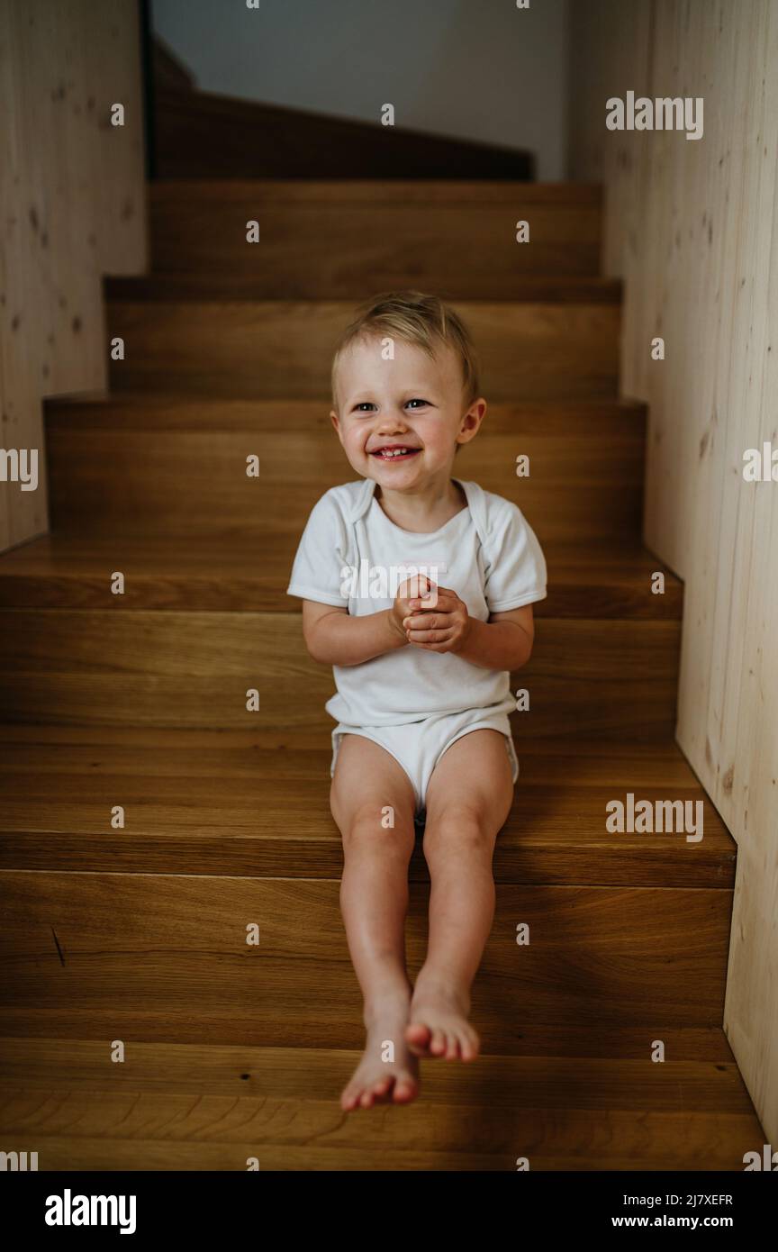 Cute little girl sitting on stairs at home and looking at camera. Stock Photo