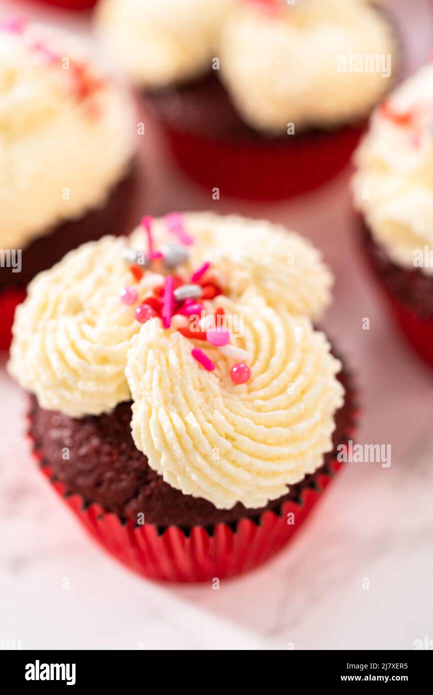 Piping white chocolate ganache frosting on top of red velvet cupcakes