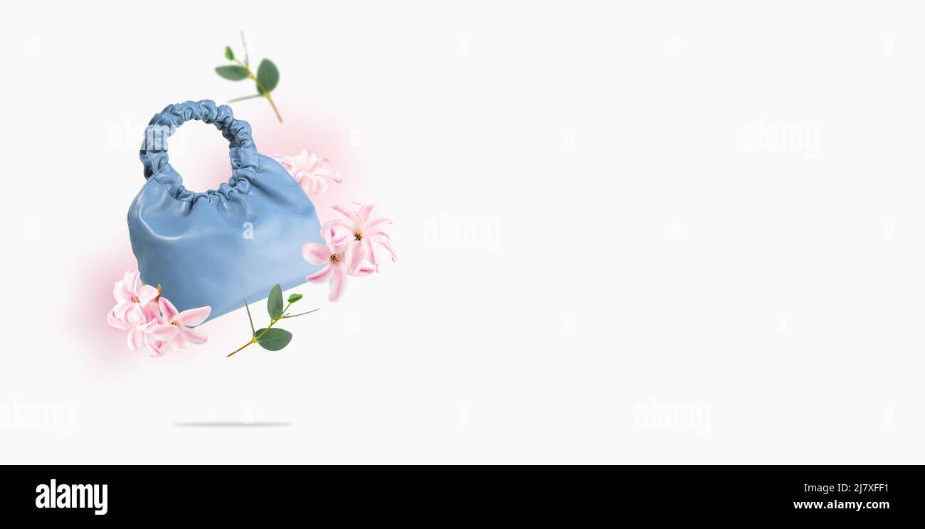 A blue eco-leather bag, leaves, flowers float on a gray background.Creative composition of flying handmade leather bag and flowers.Concept of spring Stock Photo