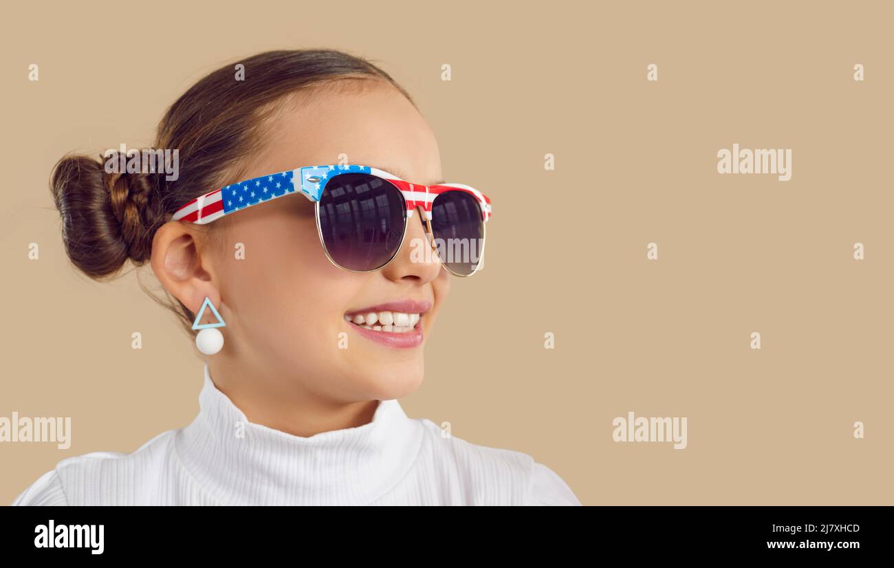 Happy girl in sunglasses with American flag design looking at copy space on studio background Stock Photo