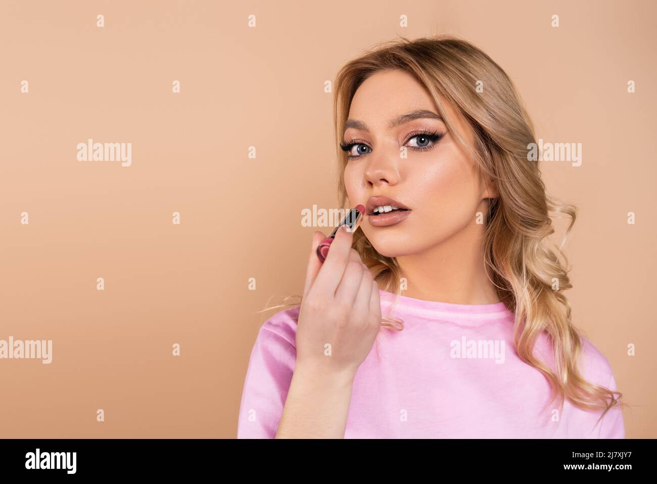 young and pretty woman applying lipstick isolated on beige Stock Photo