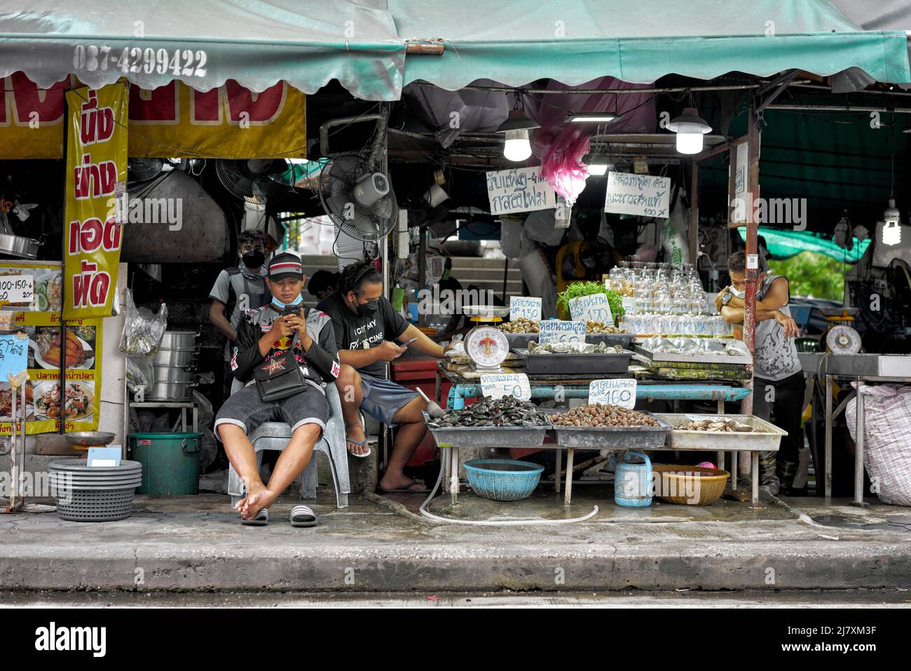 Slow days business Thailand street market staff occupied with their smartphones on a slack business day Stock Photo