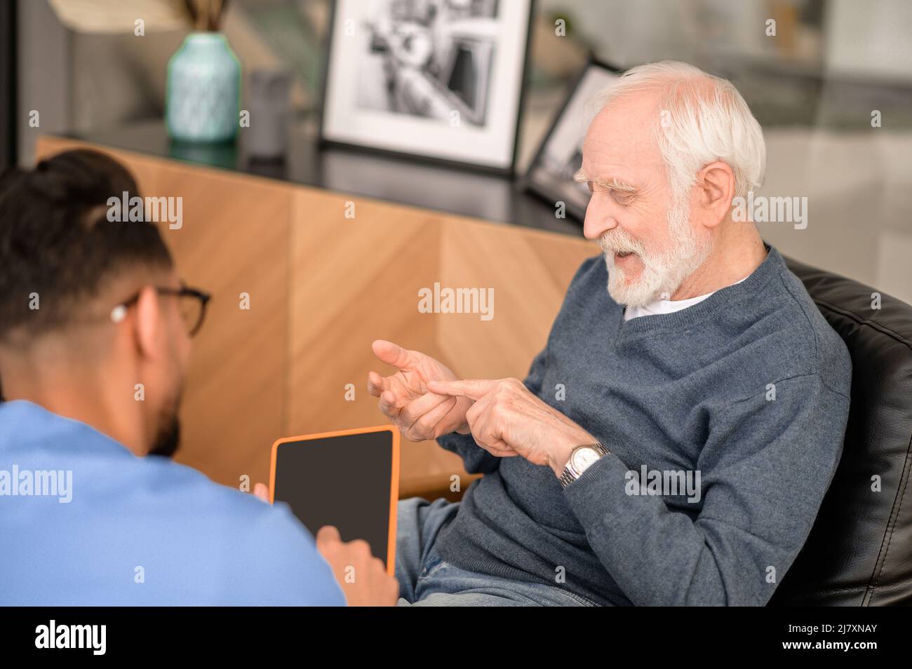 Concentrated pensioner enumerating something in conversation with his caregiver Stock Photo