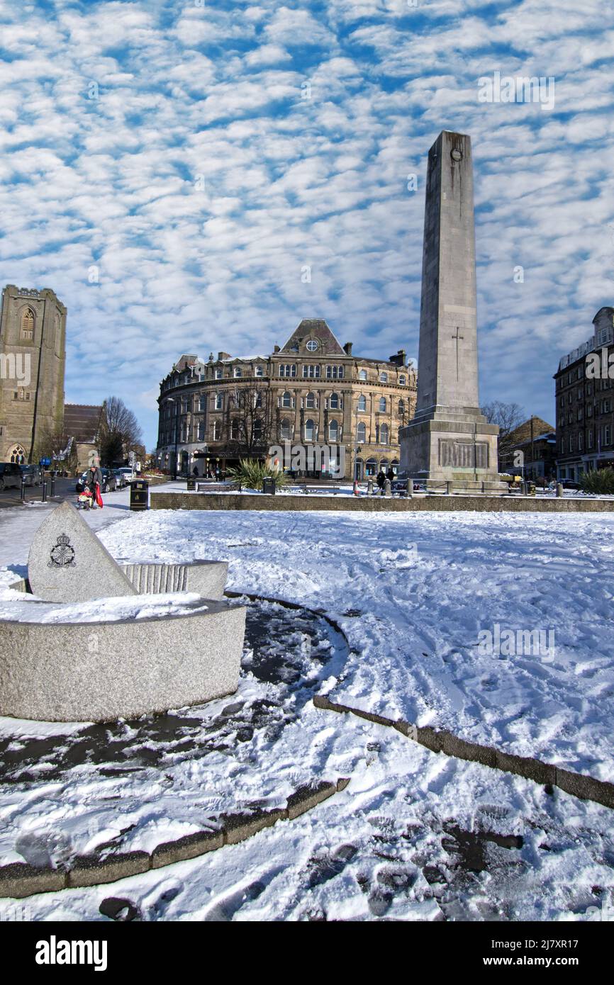 A view of Harrogate town centre on a sunny snowy winter day with The Cenotaph War Memorial a church and shops and stone Sundial in the foreground. Stock Photo