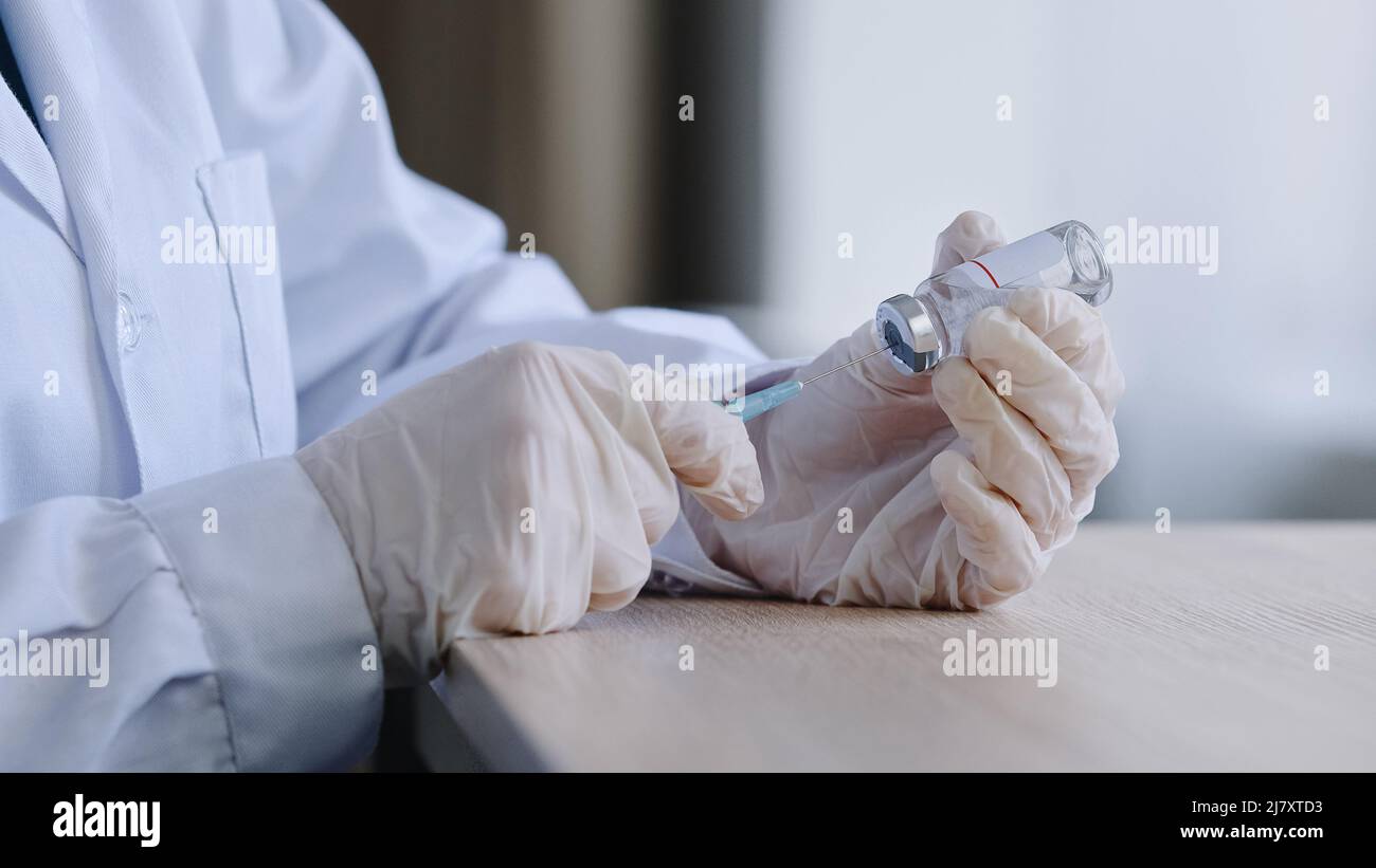 Unrecognizable female doctor pharmacist wearing latex gloves holding syringe and vial bottle of covid 19 liquid vaccine remedy cure drug preparing for Stock Photo