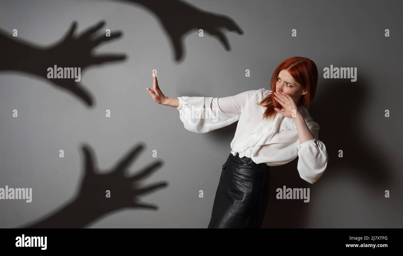 terrified woman in defensive posture is attacked by shadows of hands Stock Photo