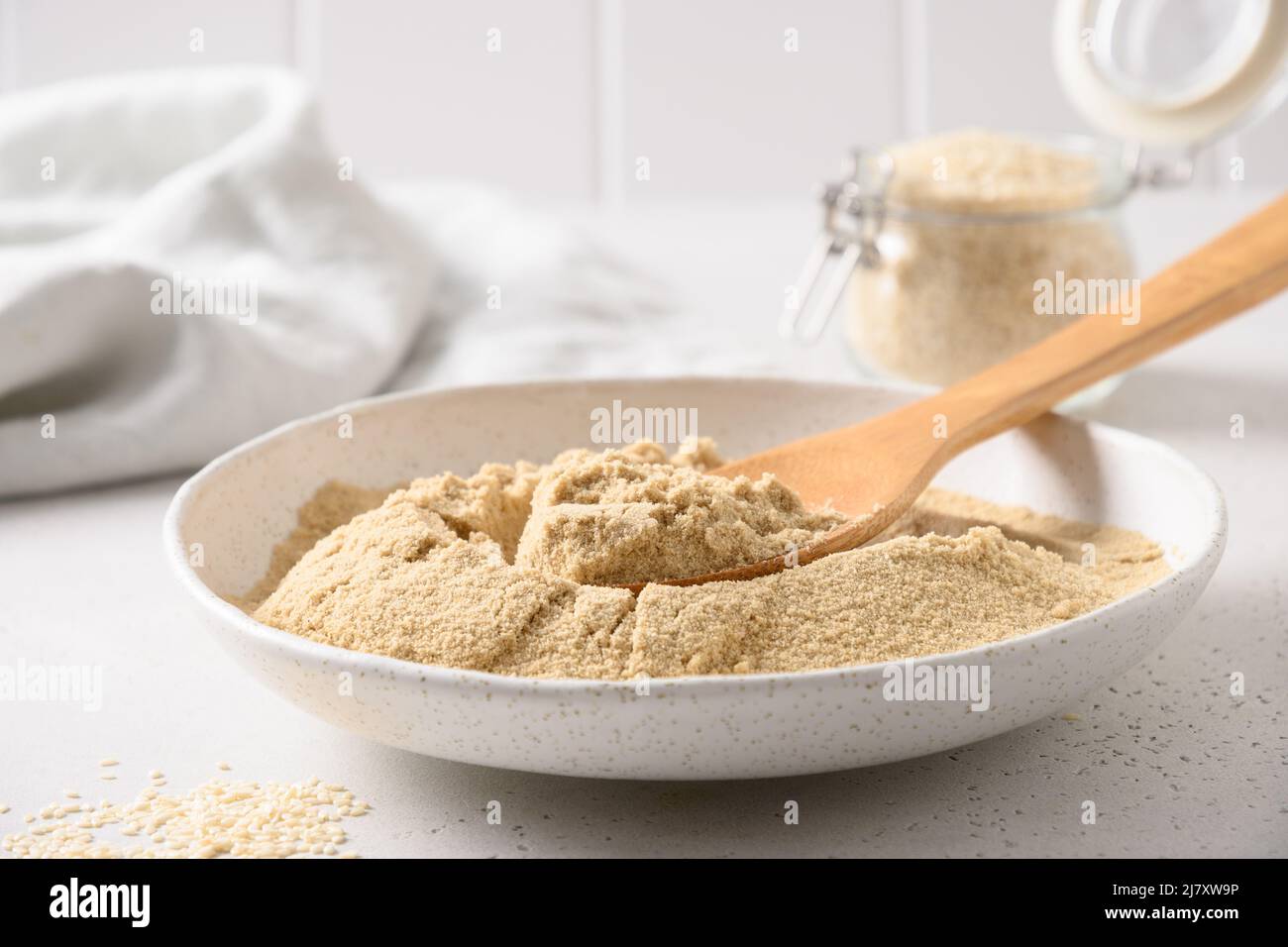 Sesame flour in white bowl on white kitchen background. Close up. Stock Photo