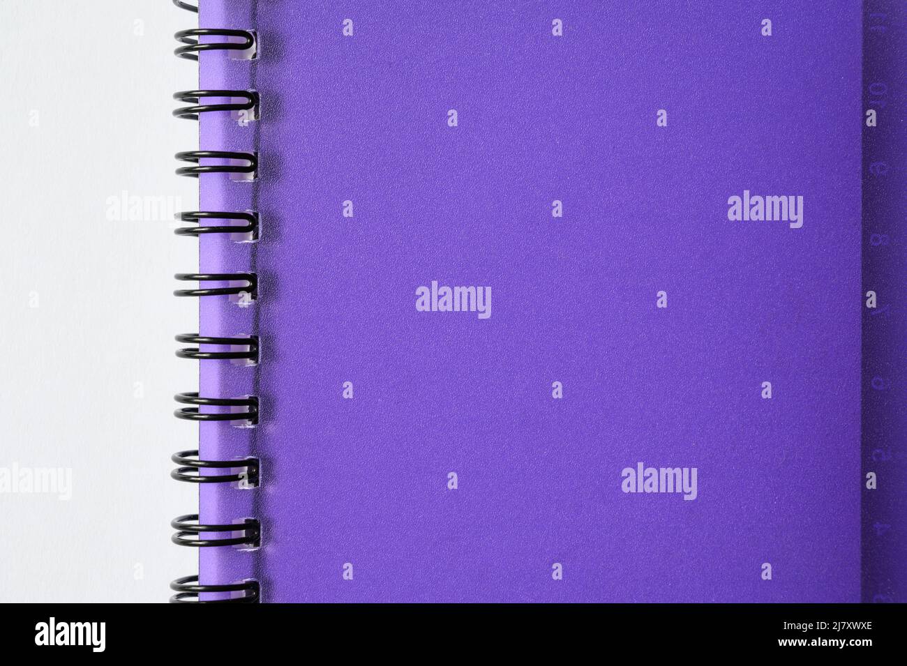Part of wirebound (or spiral bound) notebook with purple, translucent plastic cover on white background. Stock Photo