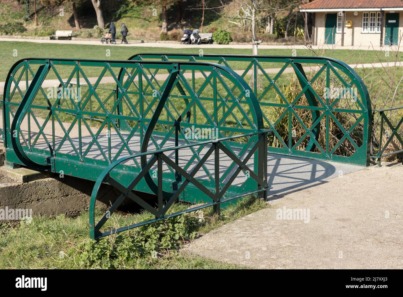 A small bridge crossing over a stream in a park with metal sides which have been painted green Stock Photo