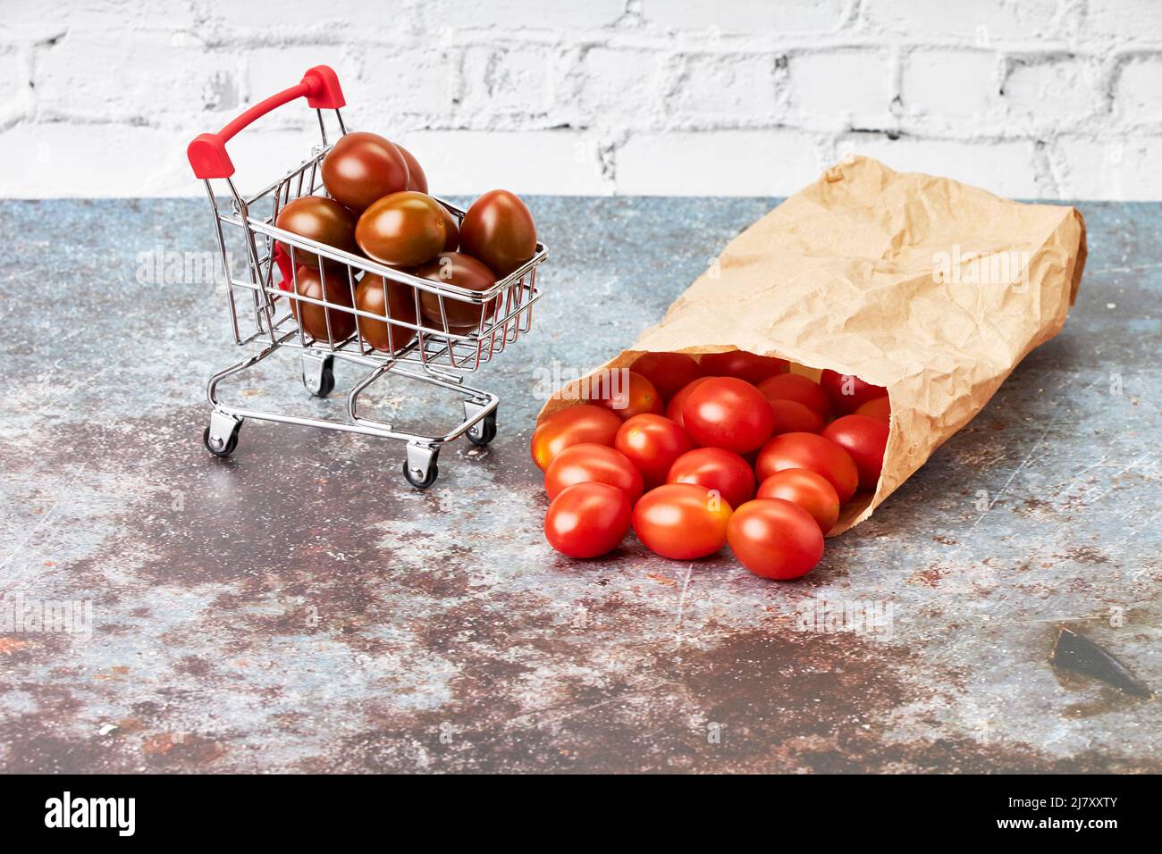 Red cherry tomatoes in a small shopping cart and paper bag. Healthy food shopping. Vegetarian and vegan food Stock Photo