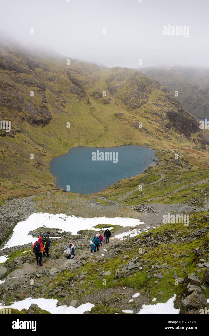 Walkers ascending the path up the north east flank of The Old Man of Coniston above Low Water in late winter the Lake District National Park, Cumbria, England. Stock Photo