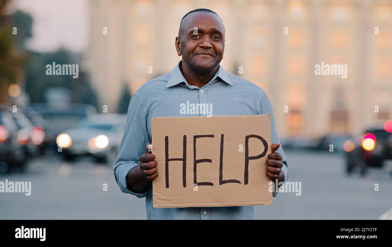 Unhappy black African American businessman holding cardboard with text help emotional pointing on sign. Stressed frustrated man hold poster looking Stock Photo
