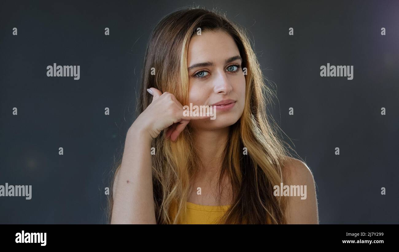 Young lady girl invites contact by phone. Playful happy pretty woman making telephone gesture near head call me sign calling symbol offering Stock Photo