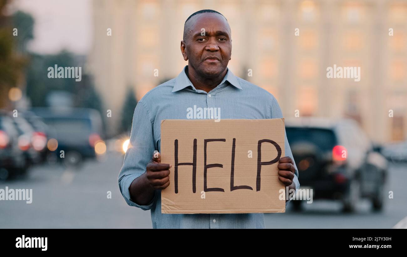 Sad stressed frustrated elderly african american poor man retirement age, lost tourist, holding cardboard banner with inscription need help asks for Stock Photo