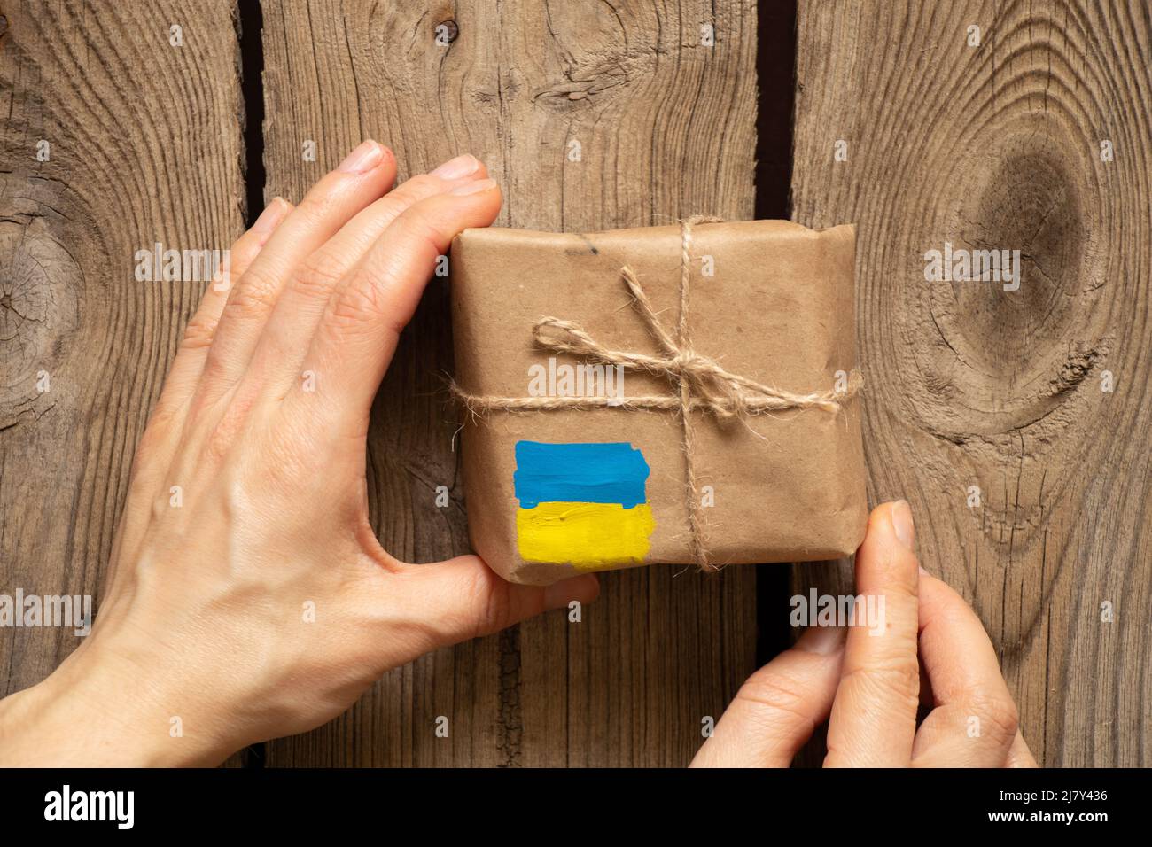 A box with a painted yellow-blue flag of Ukraine in a woman's hand, humanitarian aid for Ukraine from people Stock Photo