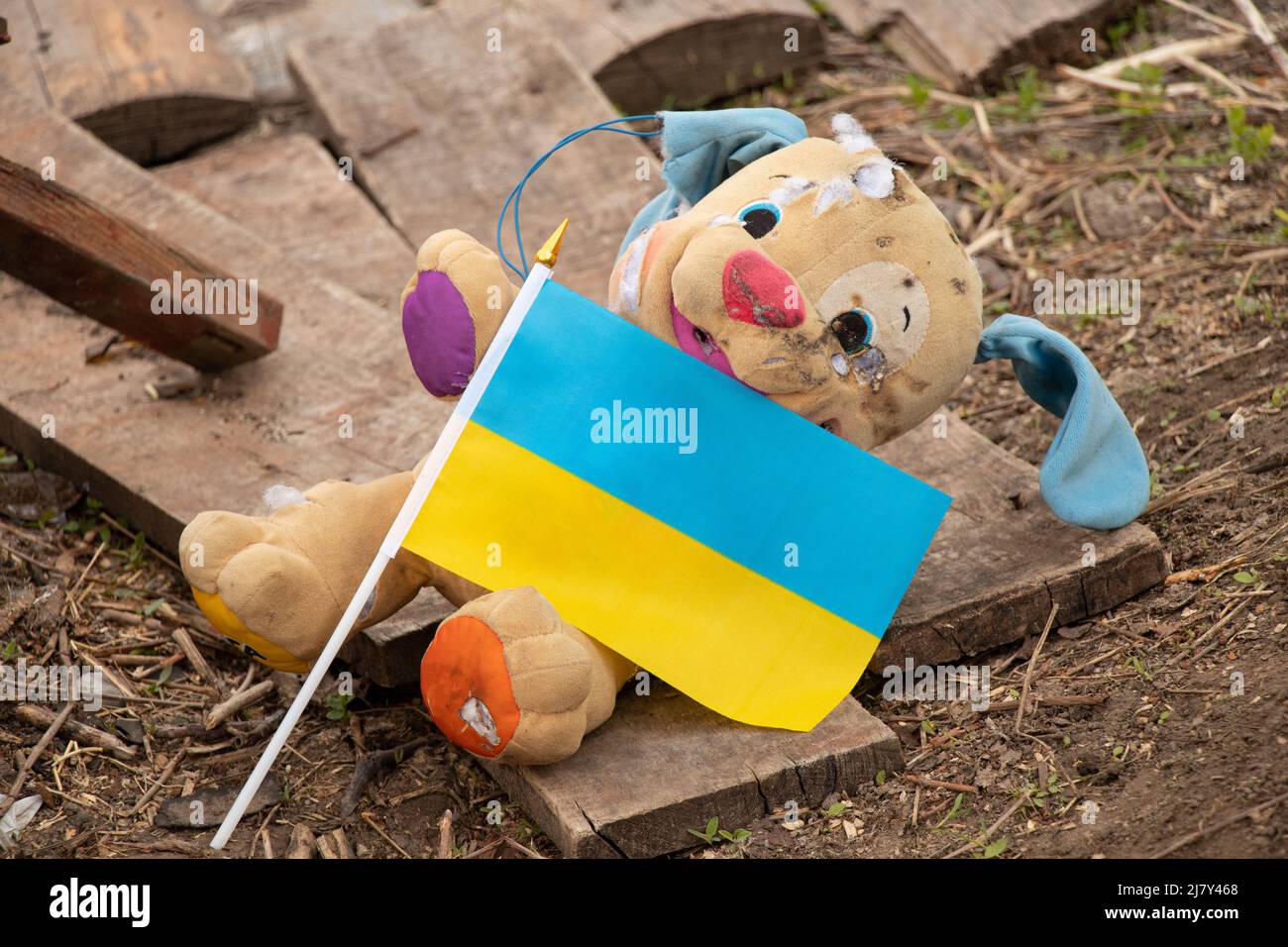 A dirty broken children's toy and the flag of Ukraine lies in the yard during the war in Ukraine, the death of children at the hands of Russian soldie Stock Photo