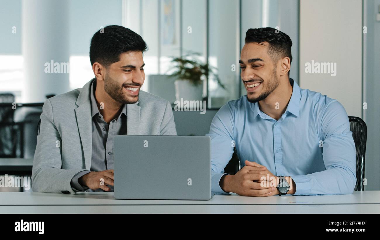 Cheerful smiling male colleagues employees cooperating in office talking working together at workplace, optimistic businessmen coworkers discussing Stock Photo