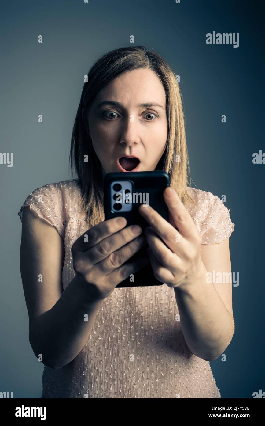 woman looks at smartphone with surprised expression Stock Photo