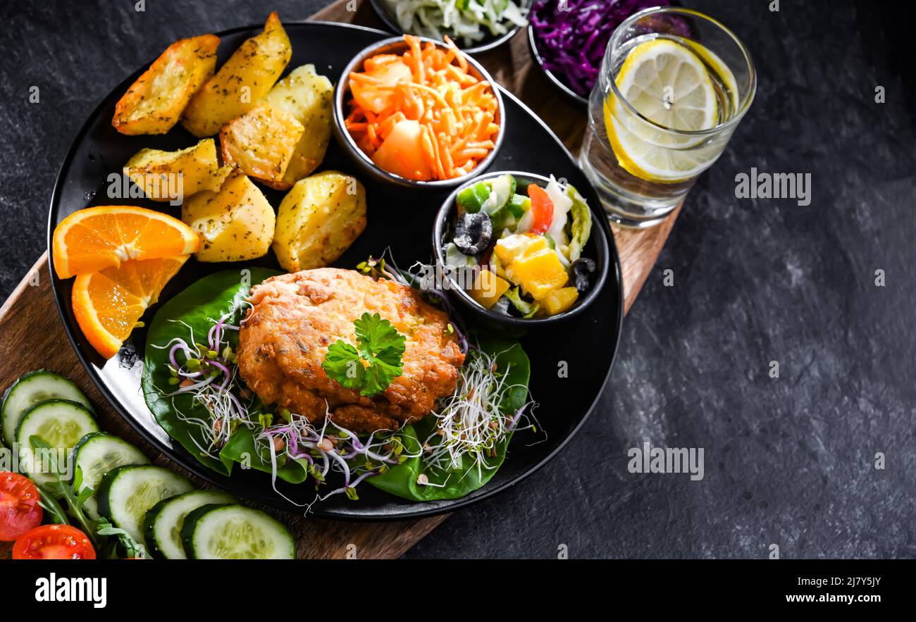 Pulled chicken cutlet coated with breadcrumbs with potatoes and vegetable salads Stock Photo